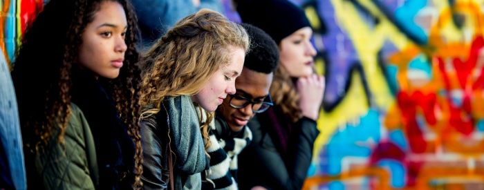 Three young people sitting in front of street graffiti 